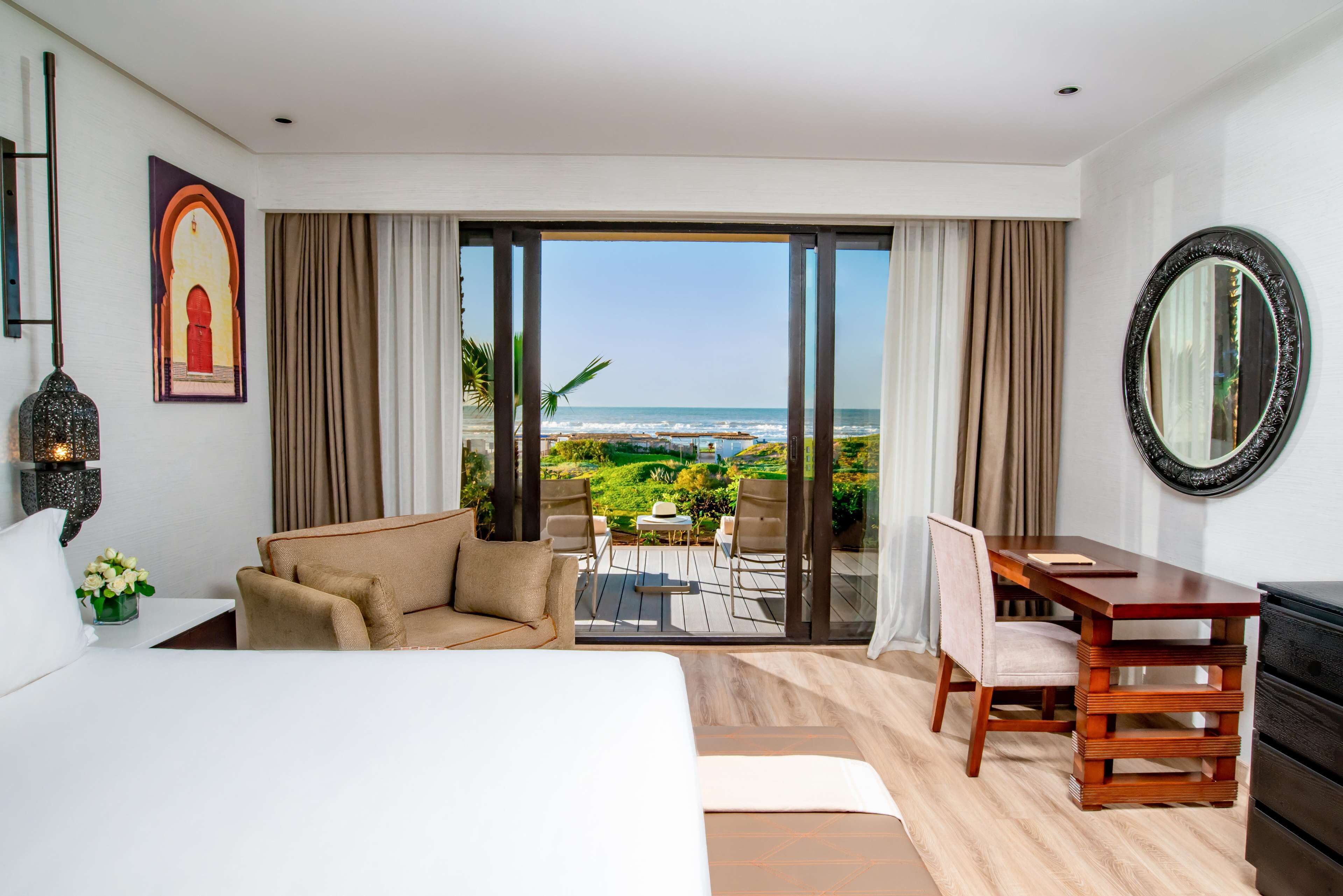 A hotel room with a bed, a desk, a chair, and a view of the ocean.