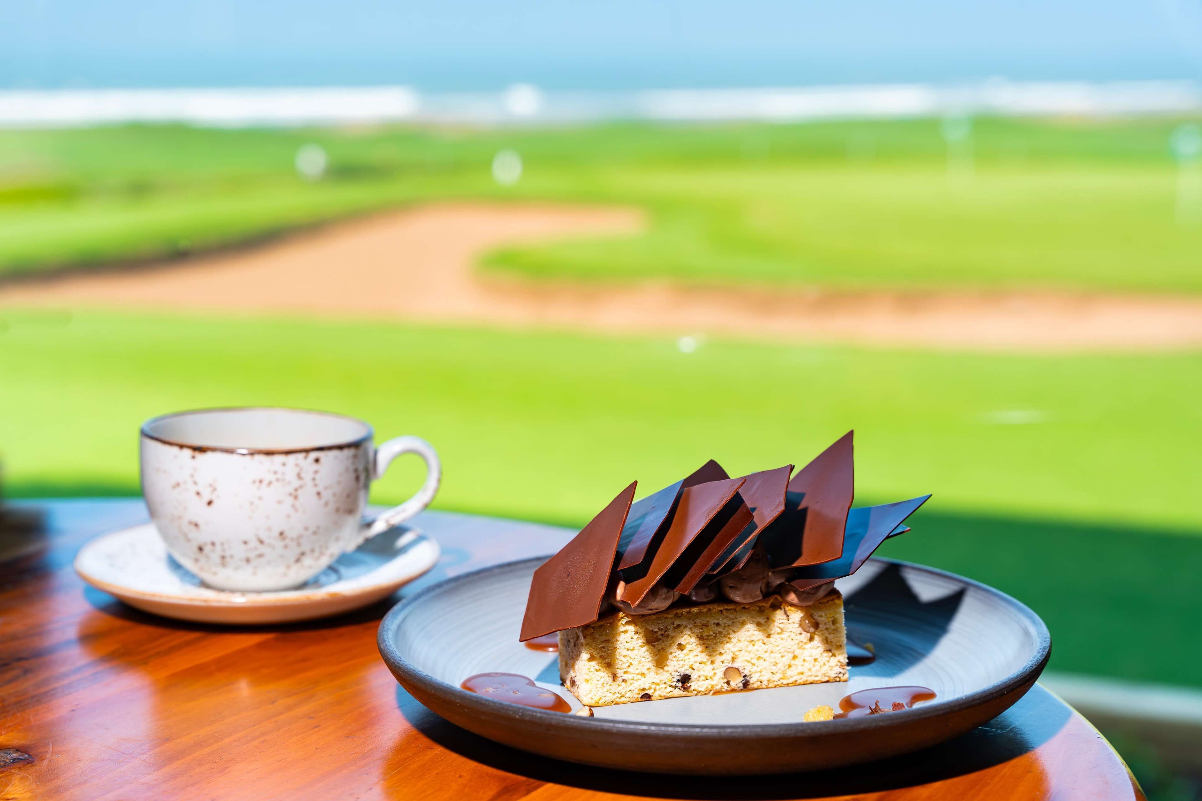 A dessert on a plate with a cup on a table, overlooking a golf course.