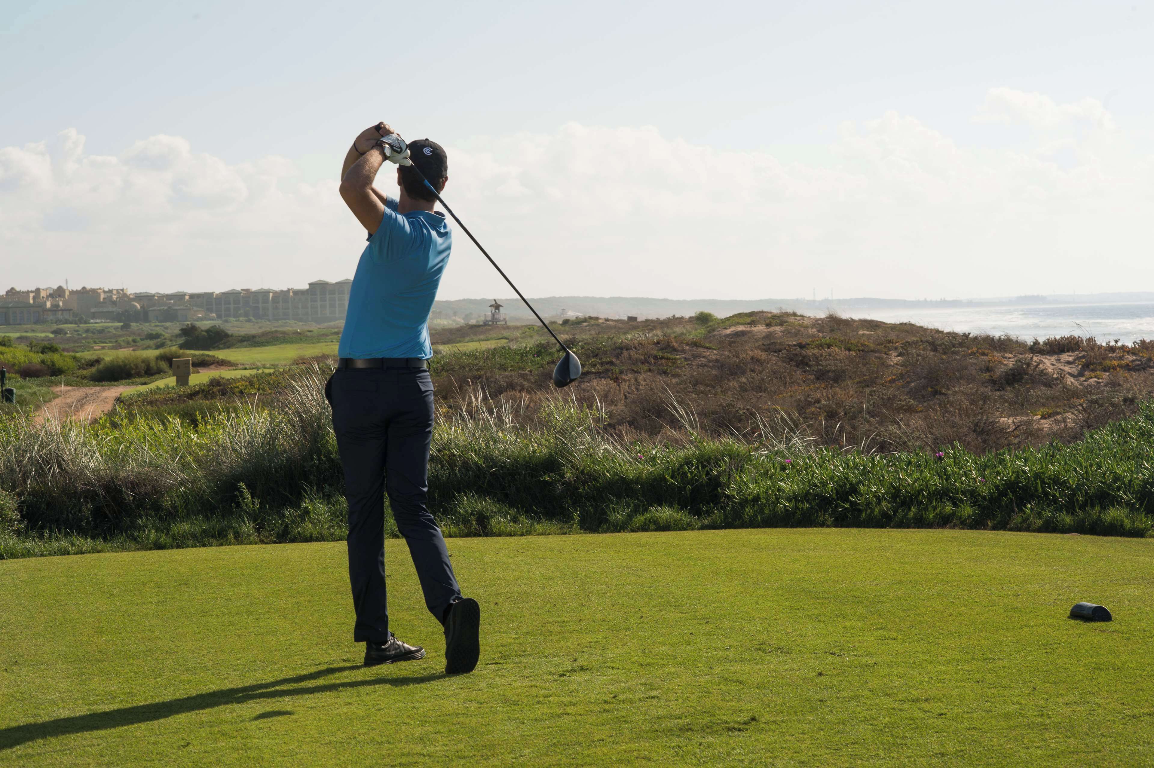 Una persona en un campo de golf con vista al mar y edificios lejanos.