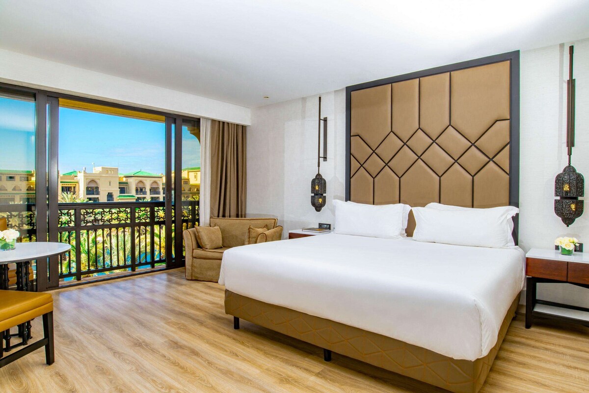 A hotel room with a large bed, a balcony with a view, a sofa, and a small table.