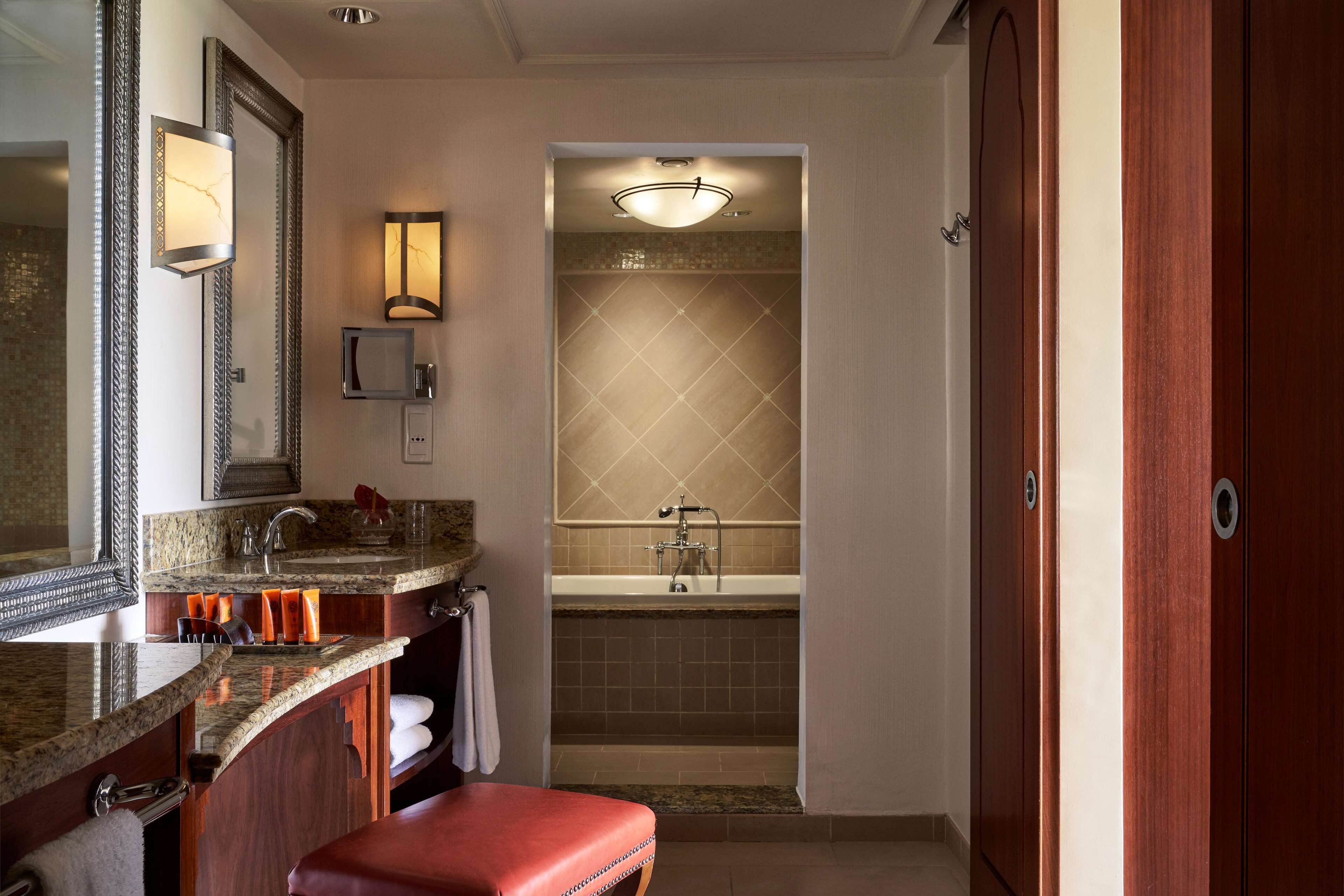 A modern bathroom with a granite countertop, a large mirror, a shower, and a wooden bench.