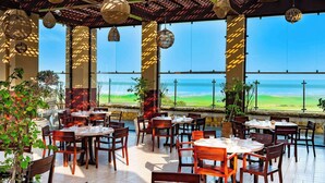 An outdoor dining area with tables and chairs, large windows, and hanging light fixtures. - Mazagan Beach & Golf Resort (El Jadida)