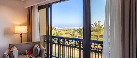 A balcony with a view of the ocean and palm trees, a sofa with a lamp, and a small table with flowers.