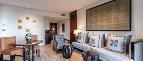 Una habitación de hotel moderna con sofá, sillas, una mesa redonda y una obra de arte abstracta de gran tamaño en la pared.