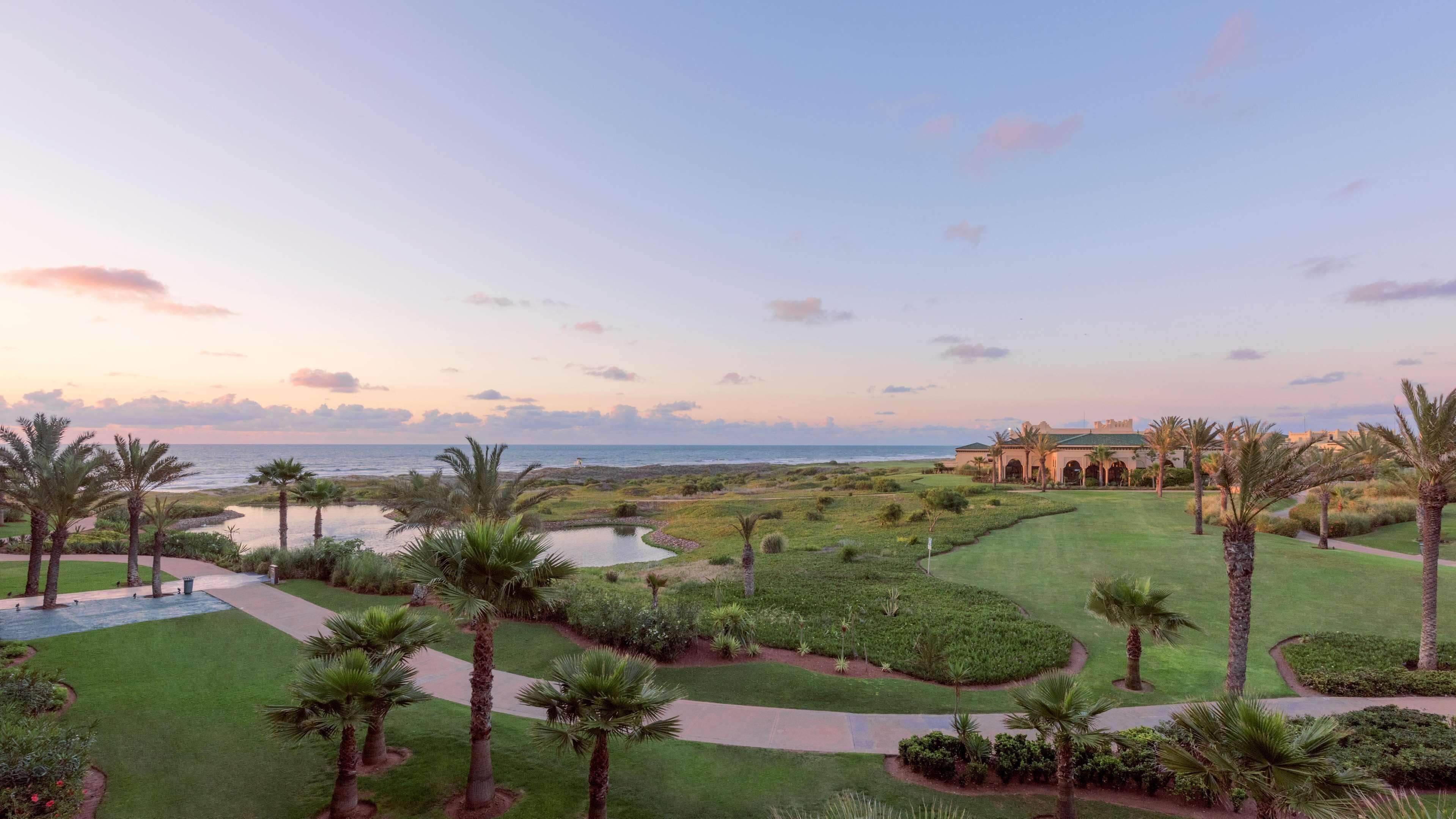 Campo de golf con vista al océano y un edificio grande al fondo.