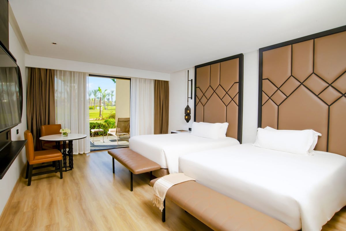 A hotel room with two beds, a bench, a dining table with chairs, and a TV.