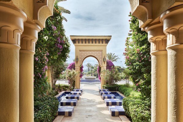 A pathway leading to a building with an archway, surrounded by lush greenery and flowering plants.