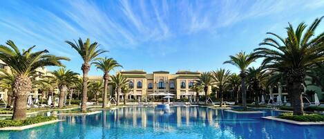Una piscina grande rodeada de palmeras y un edificio con varios balcones.