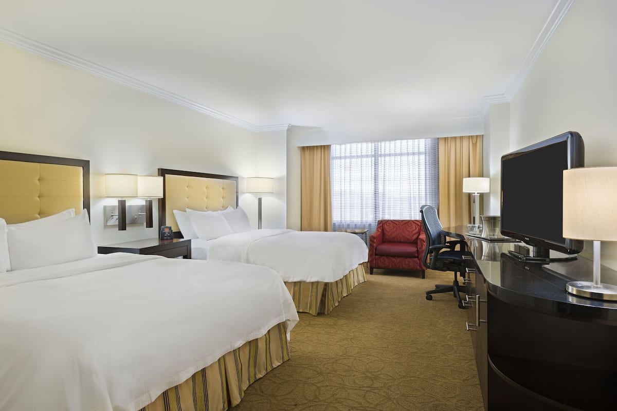 A hotel room with two beds, a TV, a desk, and a chair.