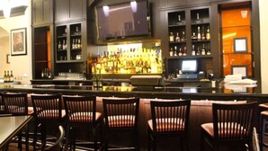 Un coin bar avec des meubles en bois foncé, un téléviseur fixé au-dessus du bar et une variété de bouteilles d’alcool exposées sur des étagères.