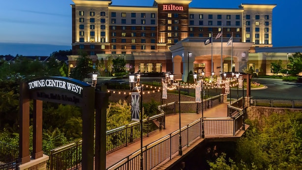 Un grand hôtel avec une enseigne « Hilton » bien visible, une passerelle couverte avec des garde-corps et une pancarte indiquant « Towne Center West ».