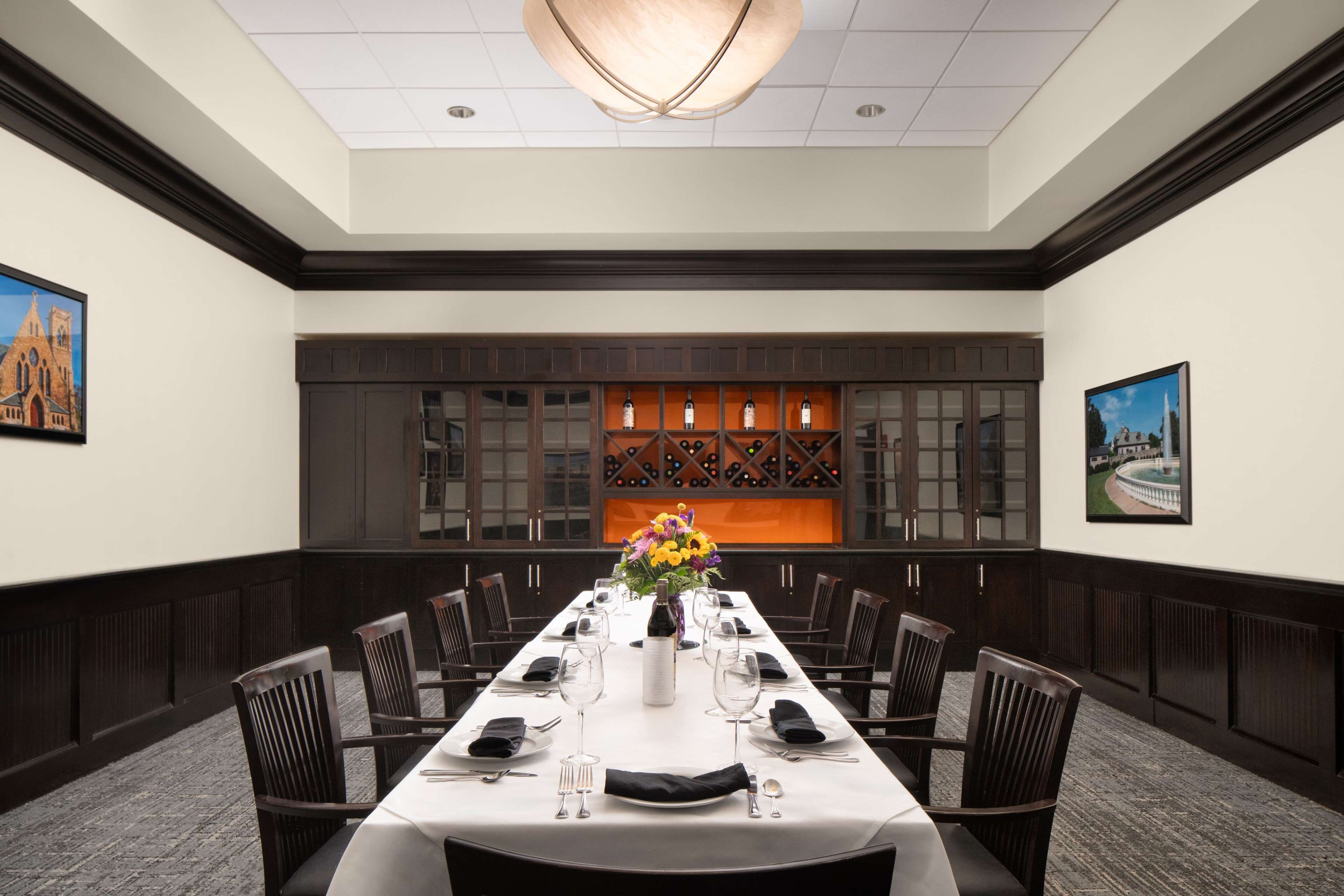 A conference room with a long table, chairs, a chandelier, and framed pictures on the walls.