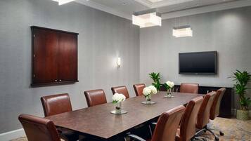 A conference room with a long table, leather chairs, a flat-screen TV, and decorative plants.