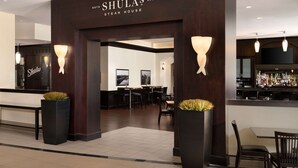 L’entrée du restaurant Shulas Steak House se distingue par sa façade en bois foncé, deux grands jardinières ornées de verdure et un bar visible sur la droite.