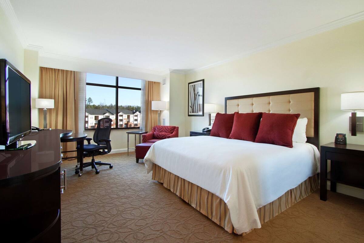 A hotel room with a large bed, a desk with a chair, a TV, and a window with curtains.