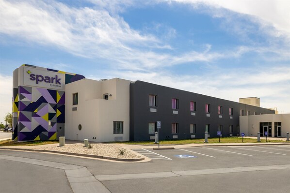 A modern hotel with a geometric facade, a parking lot, and clear skies. - Spark by Hilton Artesia (Artesia)
