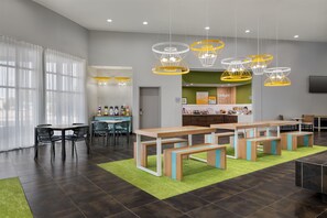 A modern dining area with wooden tables and benches, a bar area, and a green carpet. - Spark by Hilton Artesia (Artesia)
