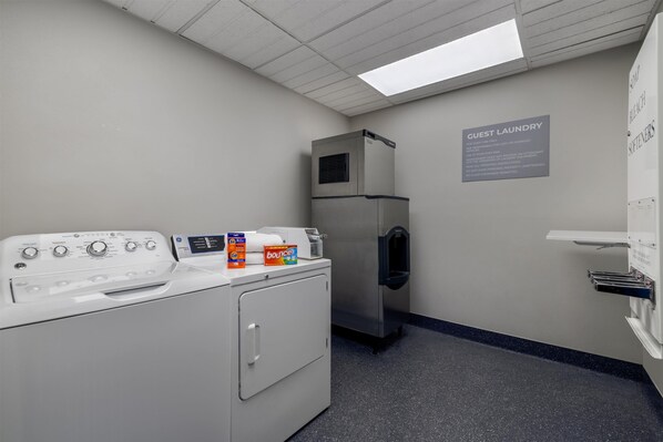 A laundry room with a front-loading washer, a stacked dryer, and a wall-mounted sink.