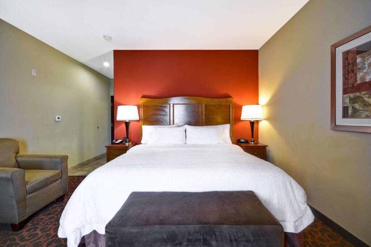 A hotel room with a large bed, two bedside tables with lamps, a chair, and a carpeted floor.