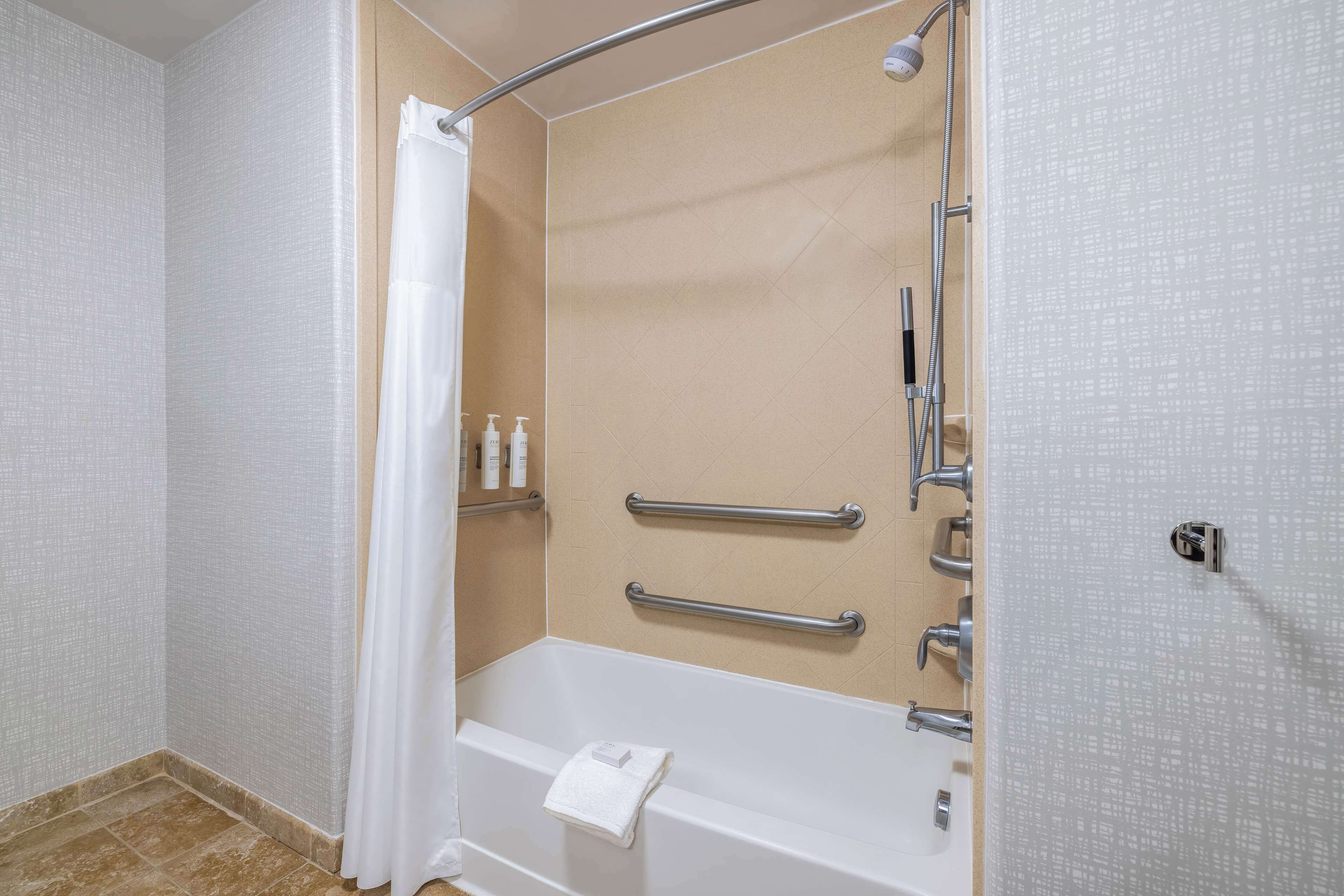 Ein Badezimmer mit Badewanne, Dusche und Handläufen.