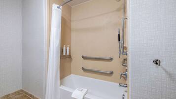 A bathroom with a bathtub, shower, and handrails.