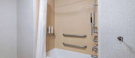 Ein Badezimmer mit Badewanne, Dusche und Handläufen.
