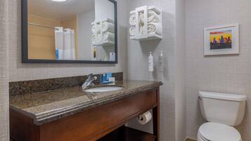 A bathroom with a granite countertop sink, a mirror, a toilet, and a towel rack.