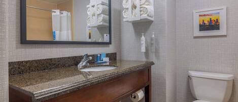 A bathroom with a granite countertop sink, a mirror, a toilet, and a towel rack.