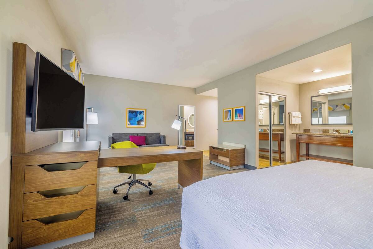 Une chambre d’hôtel comprenant un lit, un bureau, une chaise, une télévision et une salle de bain avec un miroir et des toilettes.