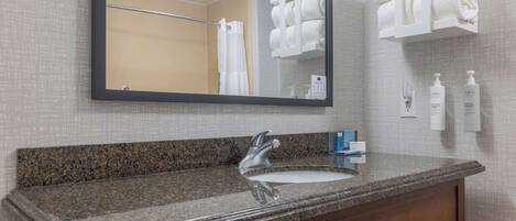 A bathroom with a granite countertop sink, a mirror, and a towel rack with folded towels.