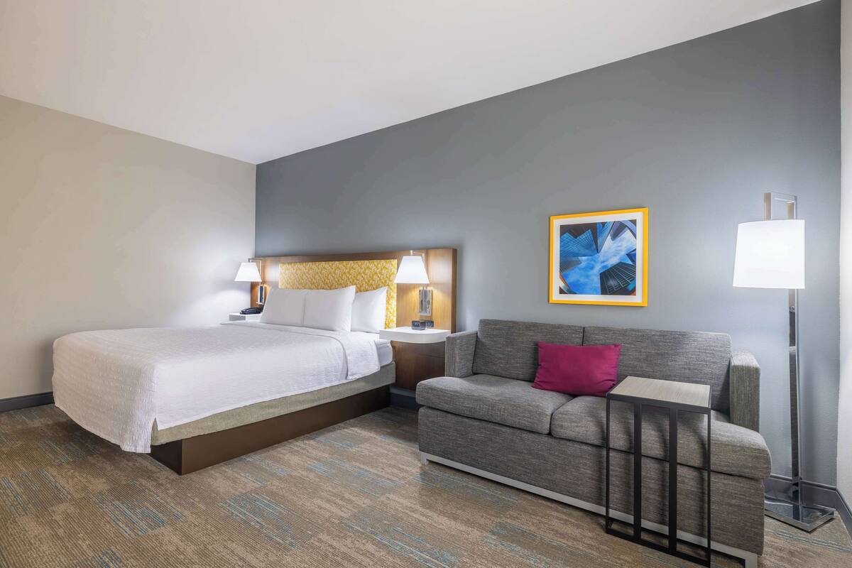 Une chambre d’hôtel avec un lit, un canapé, une petite table, une lampe et un tableau encadré au mur.