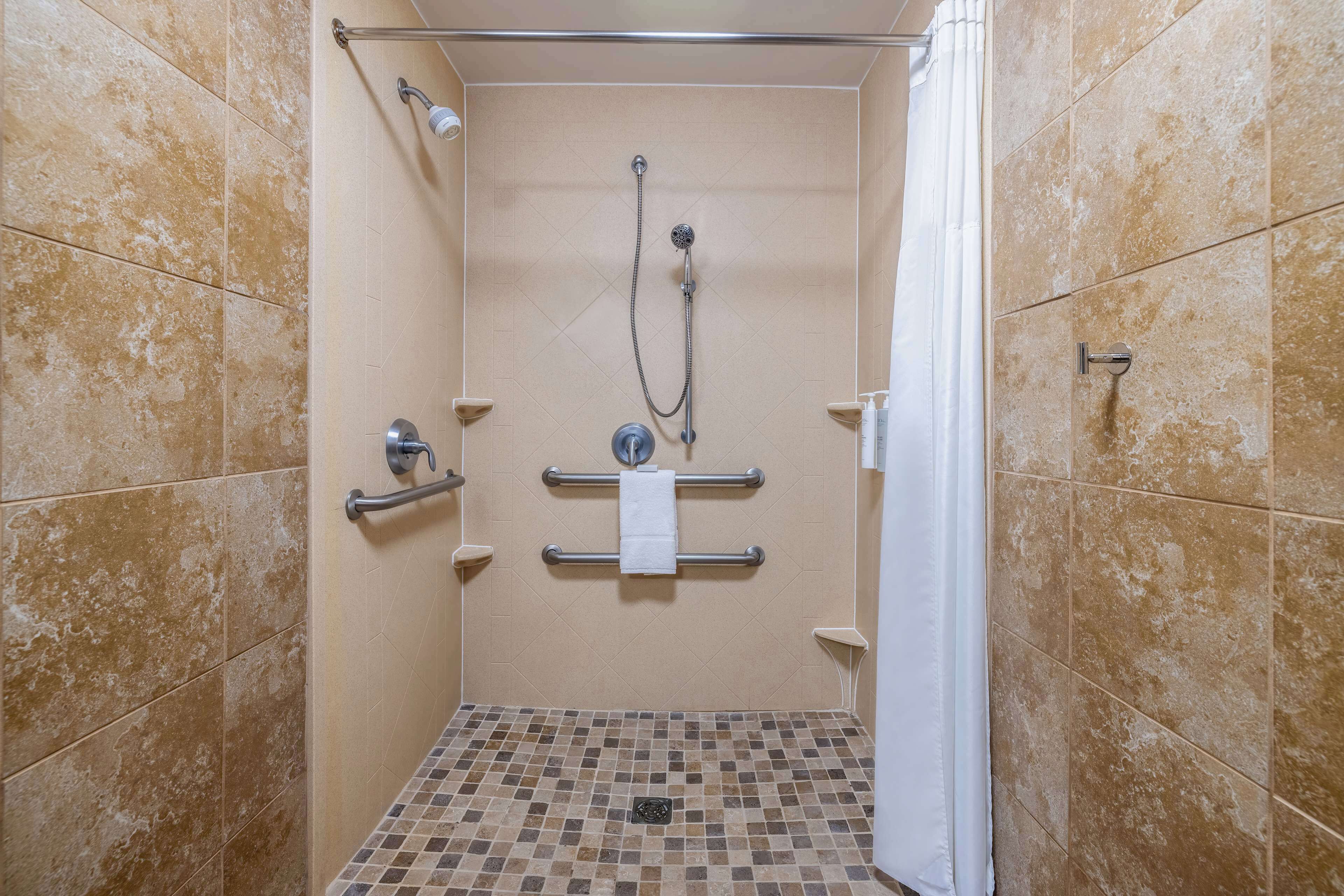 A small, tiled shower stall with a grab bar, a towel rack, and a showerhead.