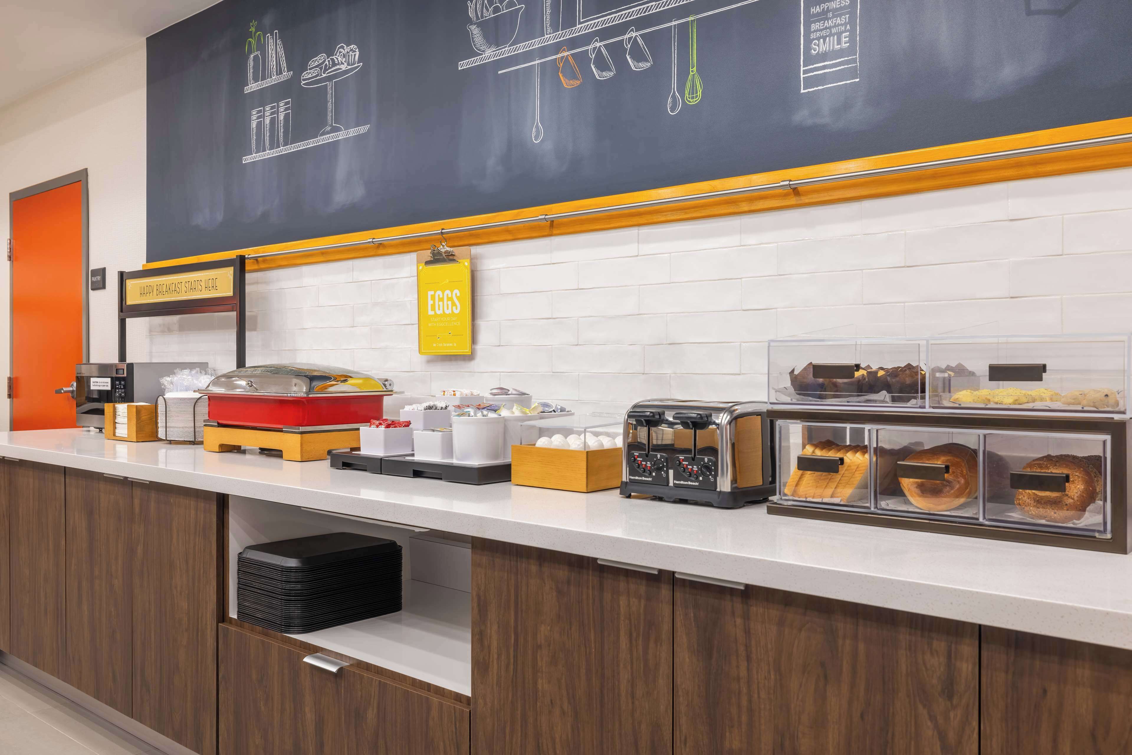 A breakfast bar with various food items, a chalkboard menu, and a sign indicating the location of the breakfast area.