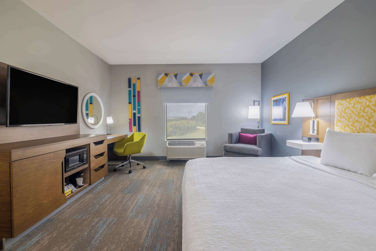Une chambre d’hôtel avec un grand lit, un bureau doté d’un téléviseur à écran plat, une chaise, une fenêtre avec vue et une table de chevet avec une lampe.