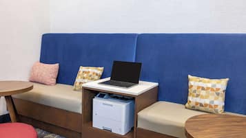 Una habitación moderna con un sofá azul, una laptop sobre una mesita y un cajón para impresora.
