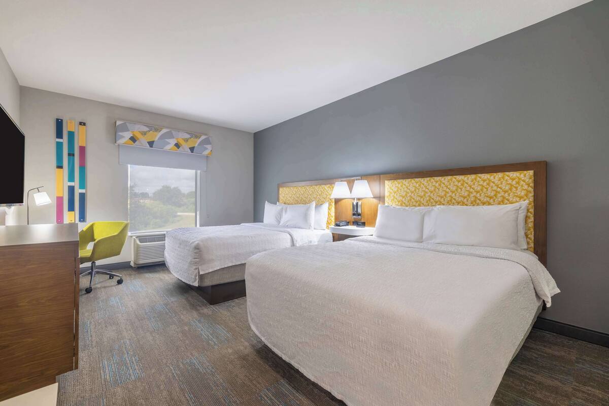 Une chambre d’hôtel avec deux lits, un bureau, une chaise et une grande fenêtre.