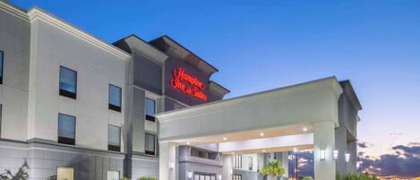 A Hampton Inn & Suites hotel with a modern facade, large windows, and a well-lit entrance.