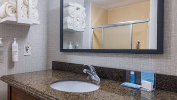 A bathroom with a granite countertop, a white sink, a mirror, and a towel rack with neatly folded towels.
