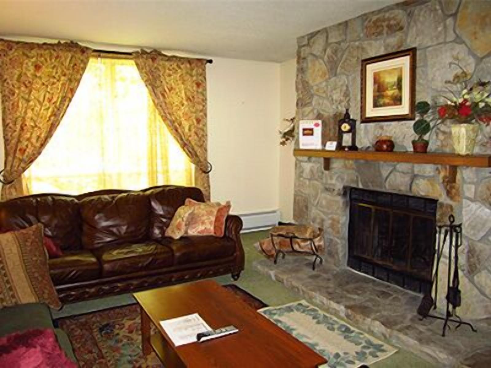 A living room with a stone fireplace, a leather sofa, and a coffee table.