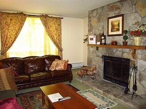 A living room with a stone fireplace, a leather sofa, and a coffee table. - Mount Snow Condominiums (West Dover)
