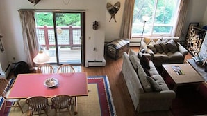 A living room with a sofa, a dining table with chairs, a fireplace, and a large window with a view of greenery. - Mount Snow Condominiums (West Dover)