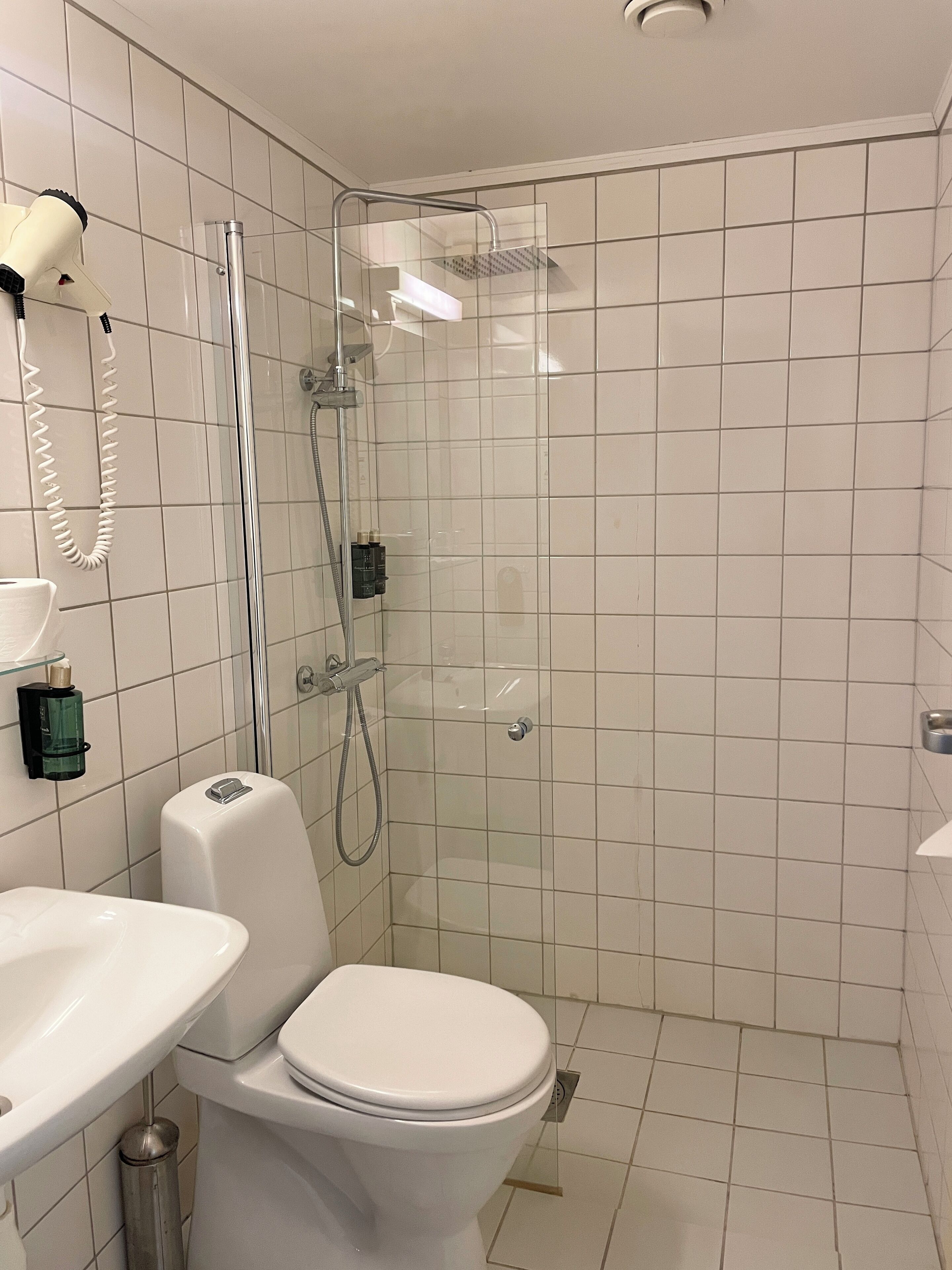Un baño moderno con inodoro, lavamanos y ducha con mampara de vidrio.