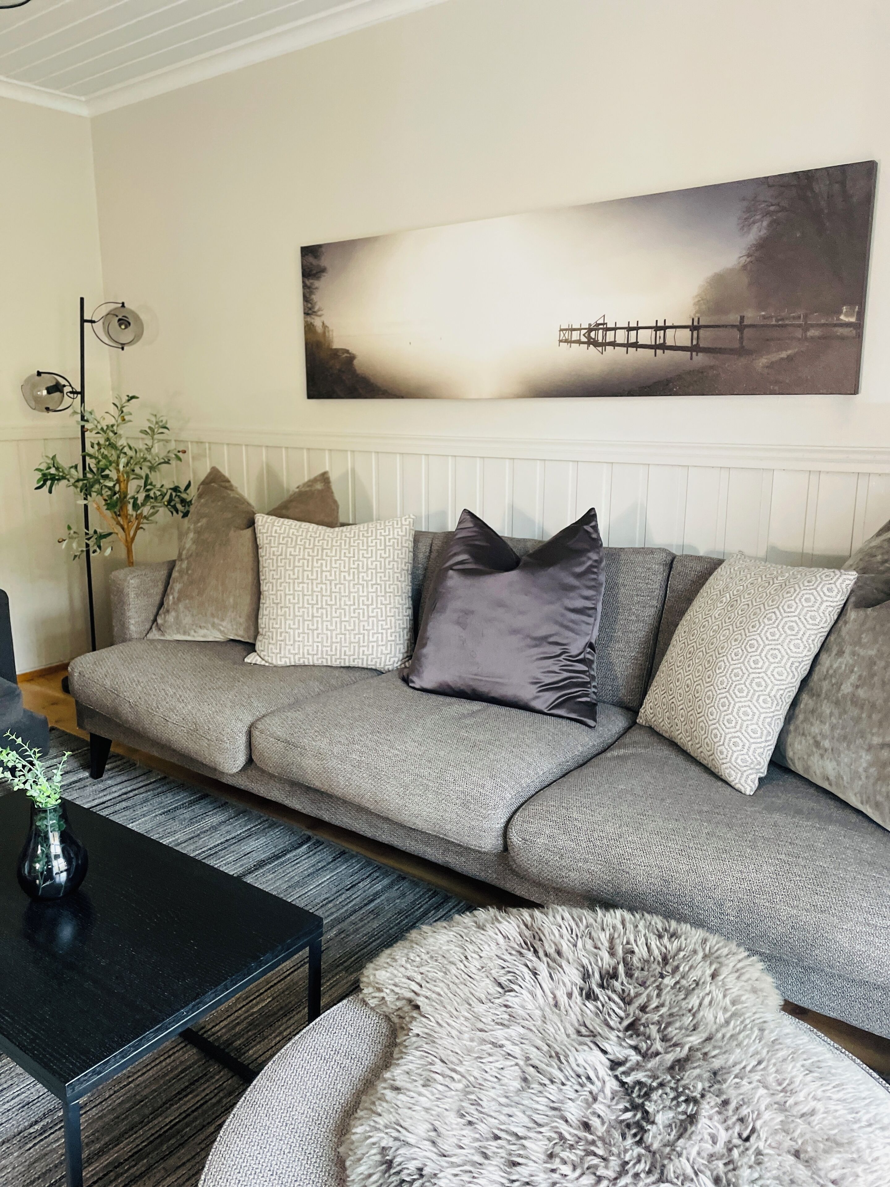 Una sala de estar moderna con un sofá gris, cojines estampados, una mesa de centro negra y una alfombra gris mullida.