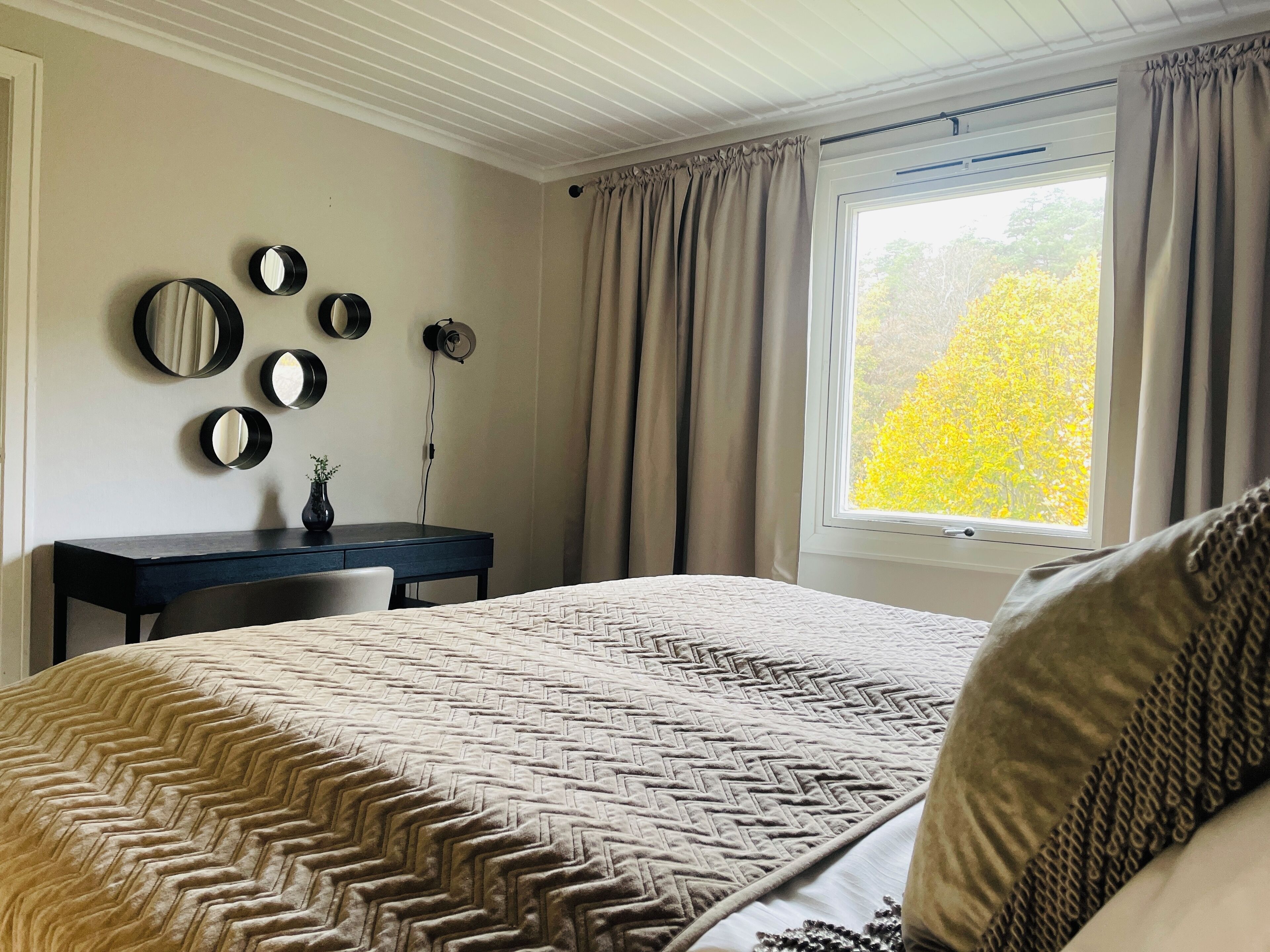 A bedroom with a bed, a desk, and a window with curtains.