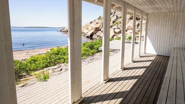 Una terraza cubierta de madera con vista a la playa y la costa rocosa.