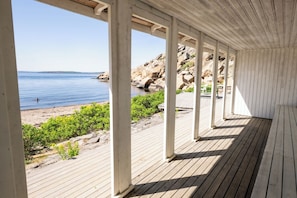 Una terraza cubierta de madera con vista a la playa y la costa rocosa.