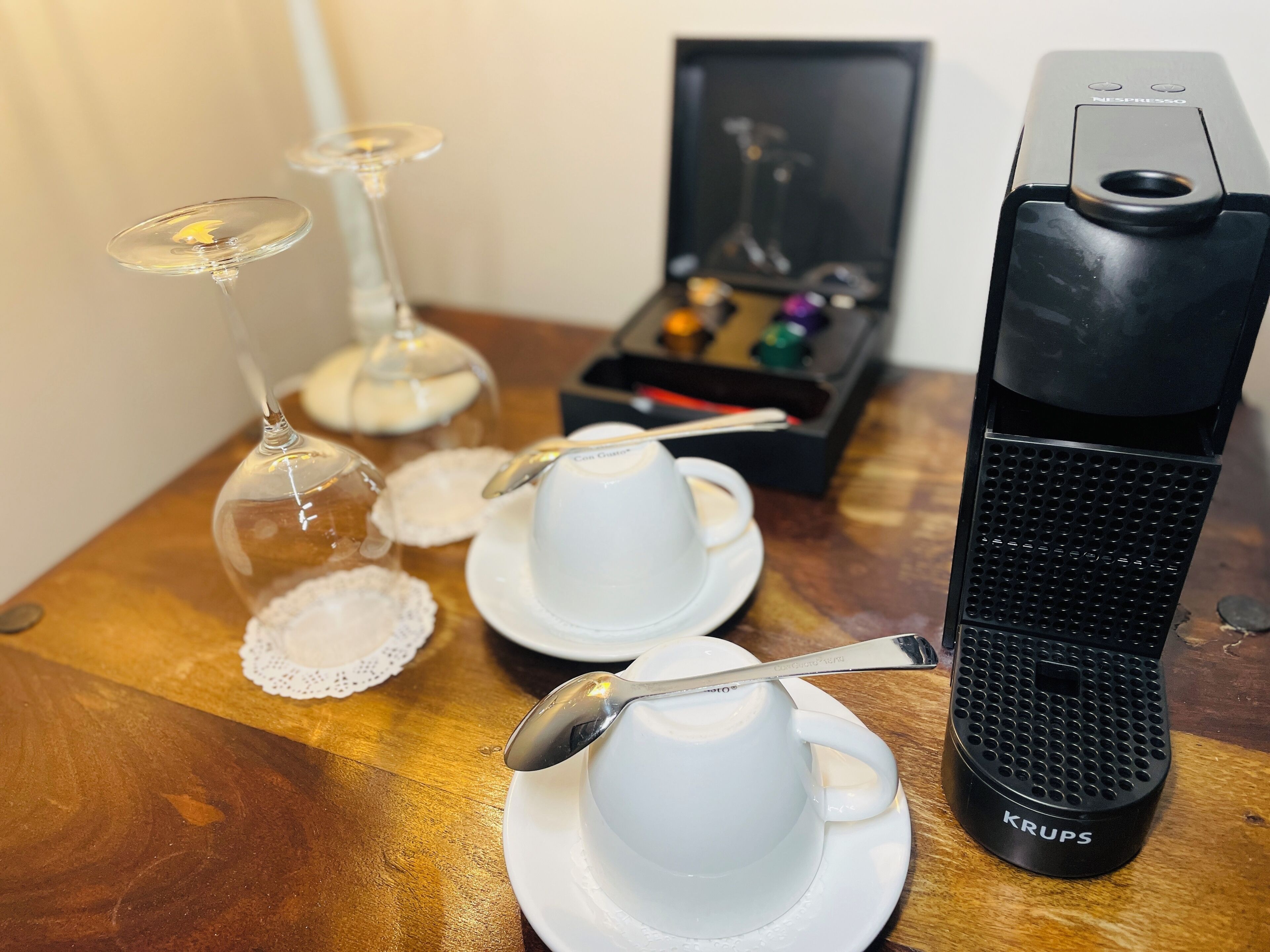 Et bord med kaffemaskine, to kopper med skeer og et glas med ske.