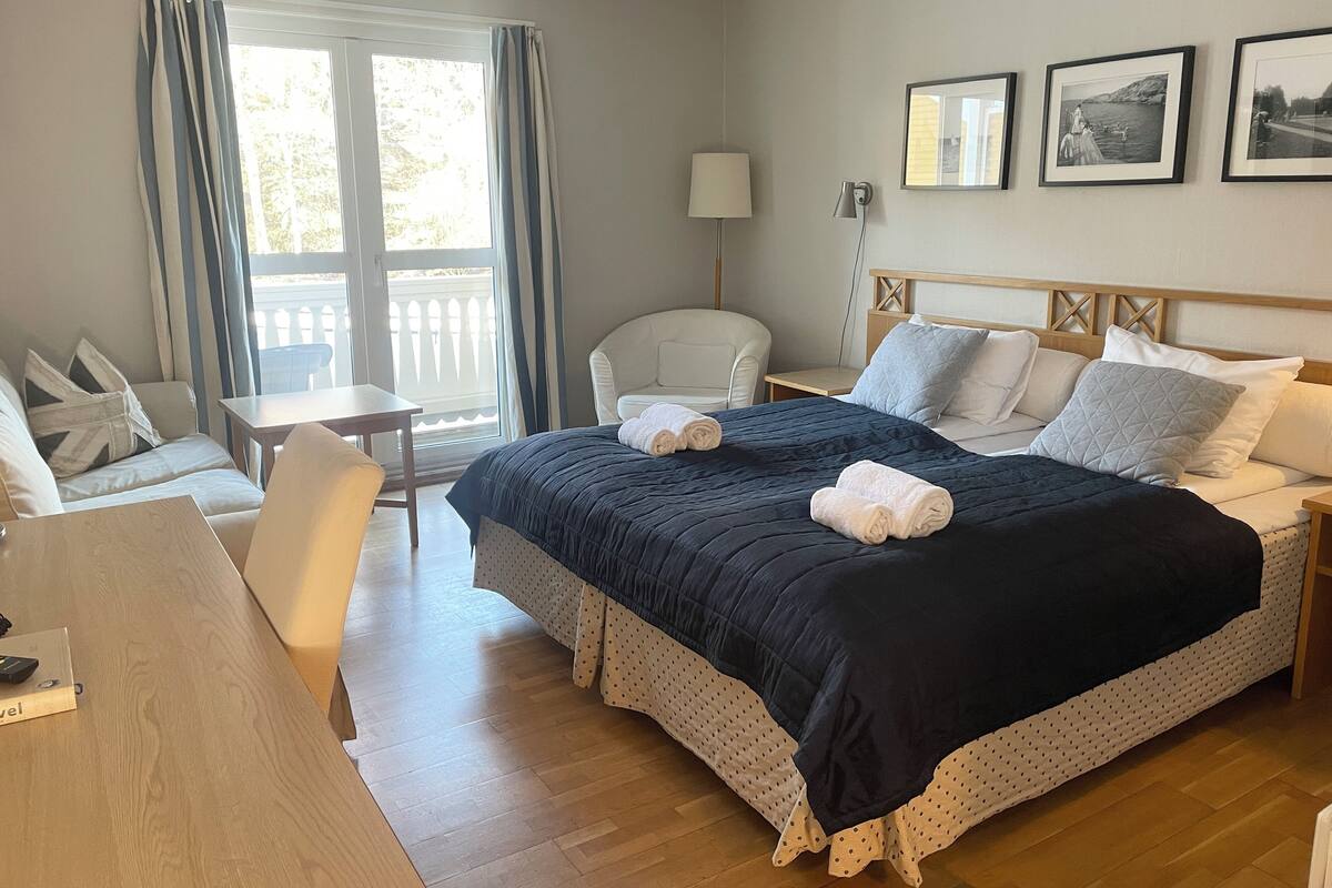 A hotel room with a large bed, a desk, a chair, and a balcony view.
