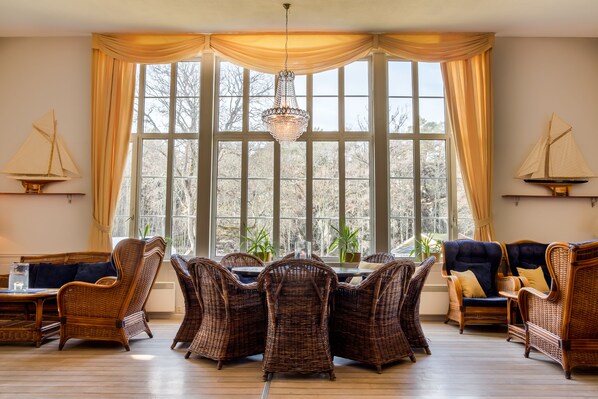 Una habitación con mobiliario de mimbre, un ventanal con cortinas y un candelabro.