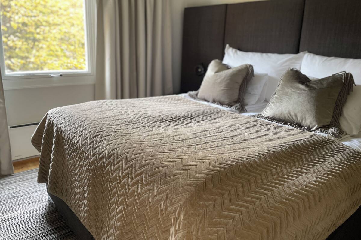 A bedroom with a large bed, a headboard, and a window with curtains.